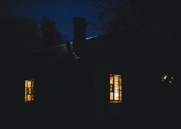 A tranquil rural house with glowing windows on a quiet night.